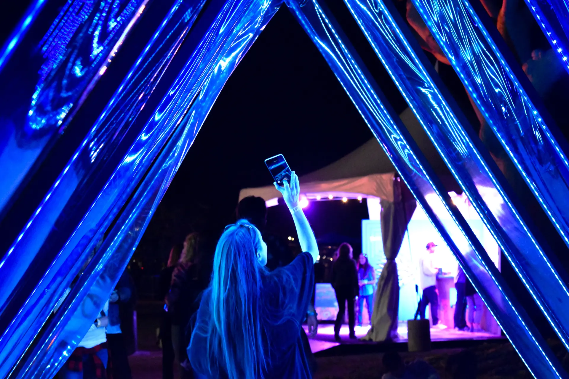 A glowing blue triangular light tunnel at night with a person taking a photo inside.