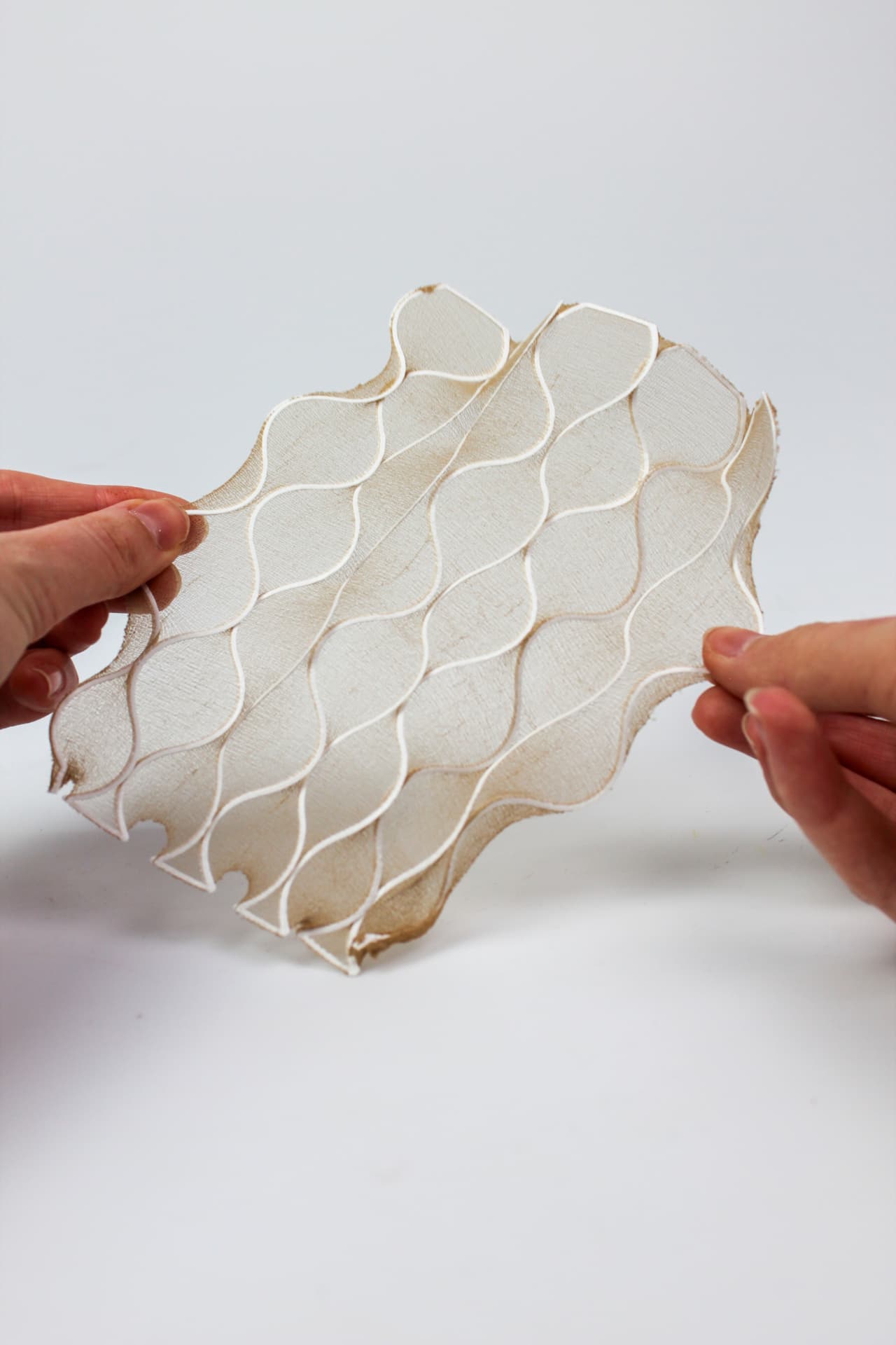Hands stretching a flat printed textile panel with a wavy line pattern.