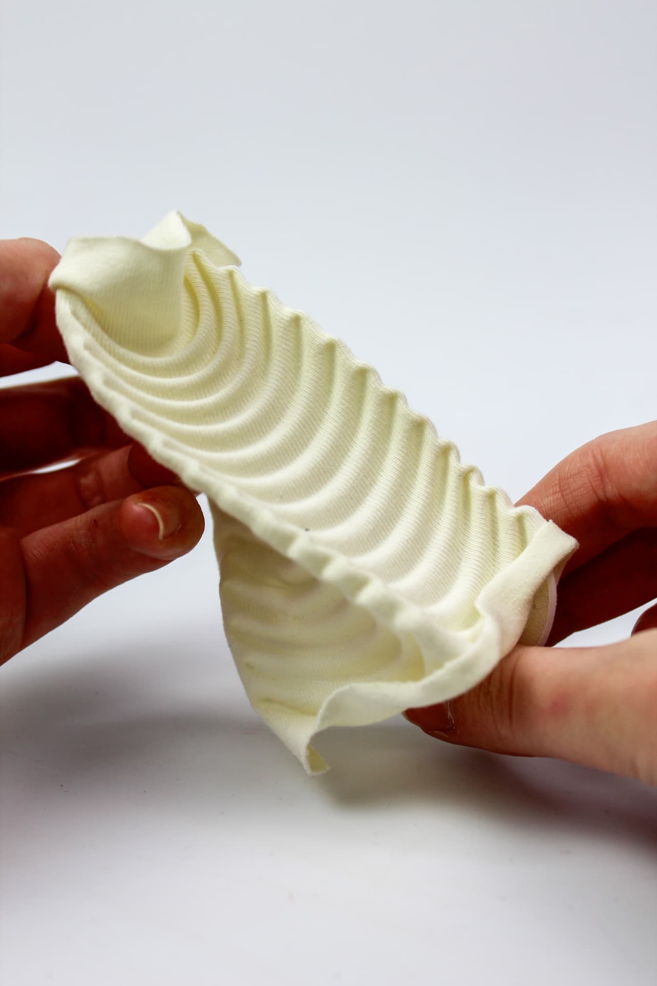 Hands holding a cream textile sample curling into concentric ribbed arcs.