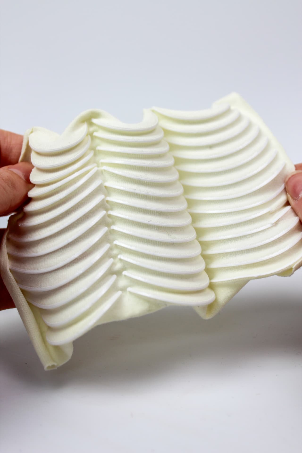 Hands stretching a cream textile panel with printed rib bands forming a chevron.