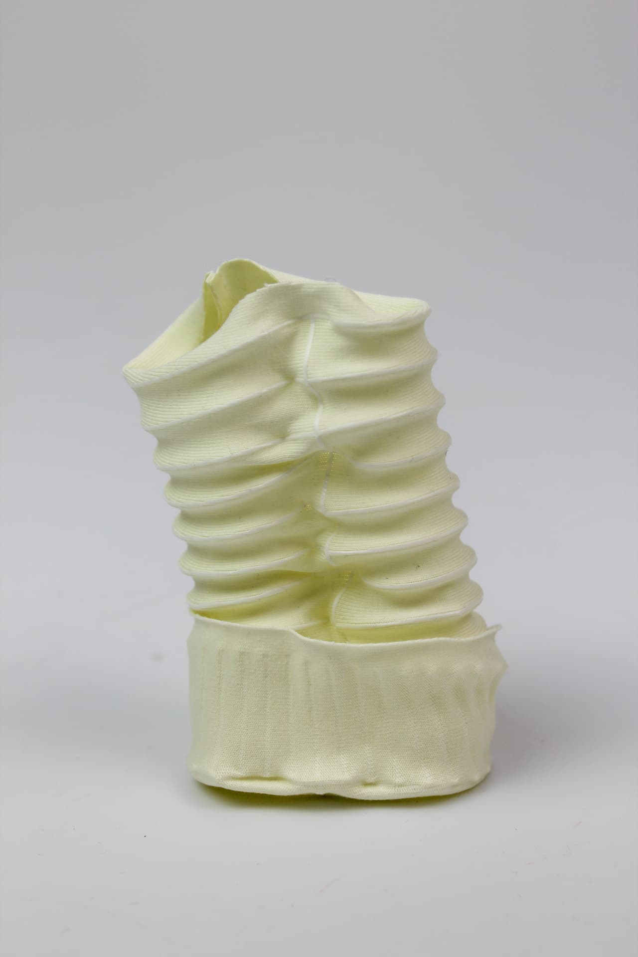Pale yellow 4D-printed textile vessel with horizontal ribbed folds.