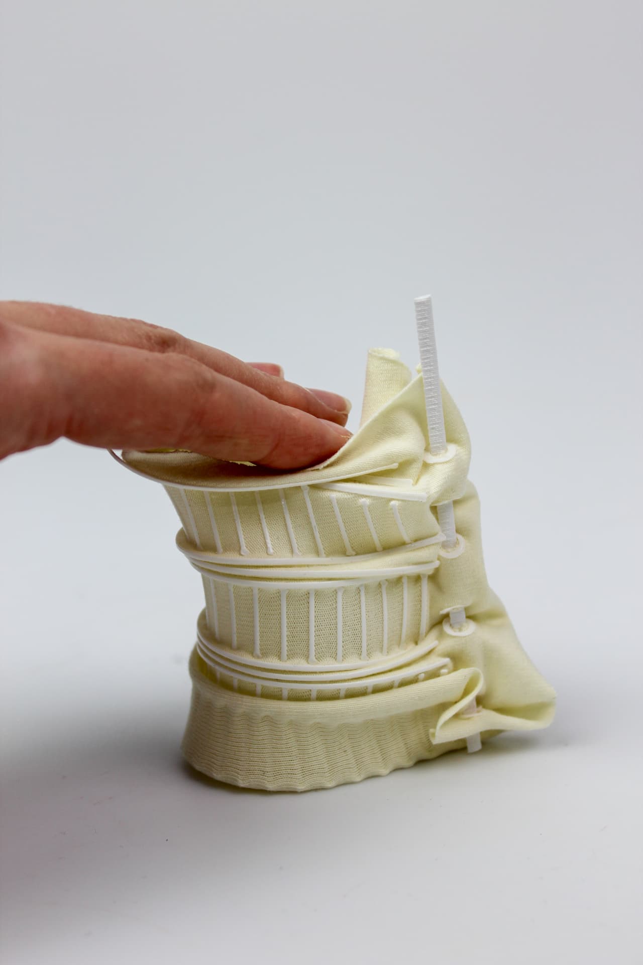 Hand opening a cream textile structure with vertical printed ribs and cinched bands.